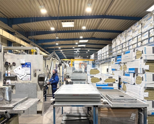 Innenansicht einer Fabrikhalle mit einem Arbeiter, der Inspektionsarbeiten durchführt. Lagerregale voller Isolationsmaterial im Hintergrund.